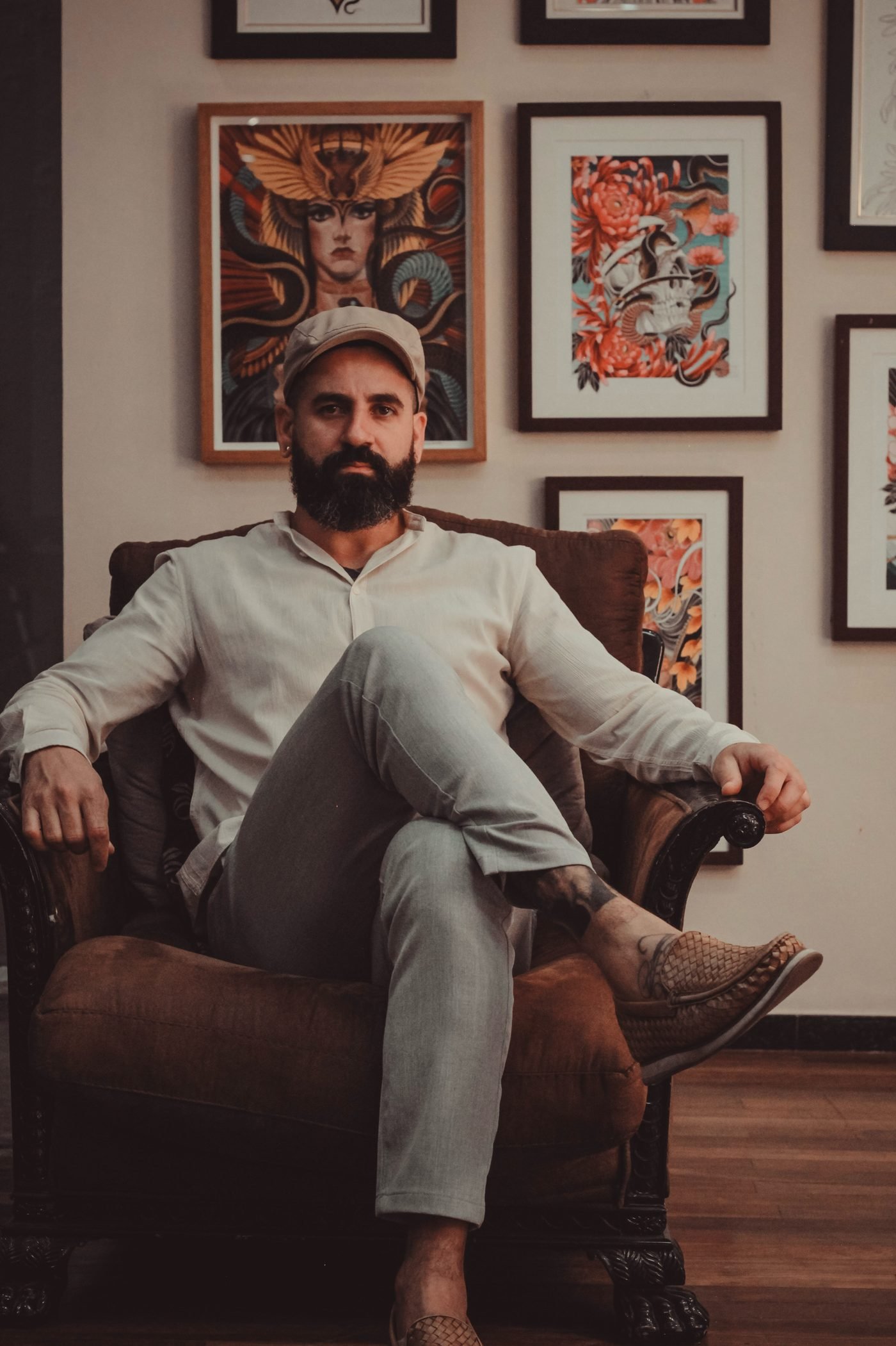 Denis Vazios sentado na poltrona do studio, cercado pelos próprios quadros